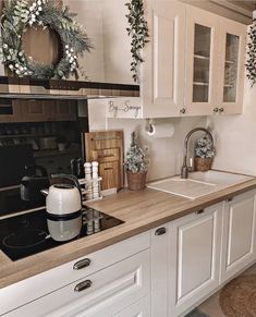 a kitchen with white cabinets and wooden counter tops, wreaths hanging on the wall