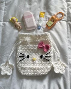 a crocheted hello kitty purse is laying on a bed next to other items