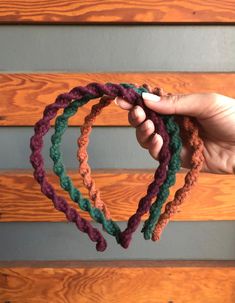 a hand holding several multicolored crocheted bracelets in front of a wooden wall