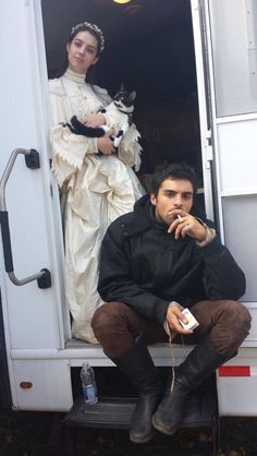 a man and woman sitting in the back of a white truck with a cat on its lap