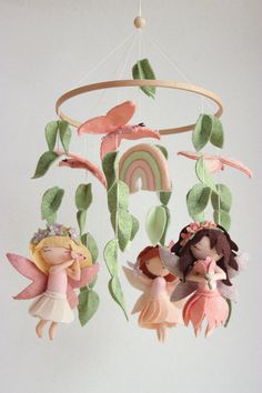 a mobile with three little fairy dolls hanging from it's sides and green leaves