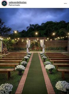 an outdoor ceremony setup with wooden benches and white flowers on the grass, surrounded by string lights