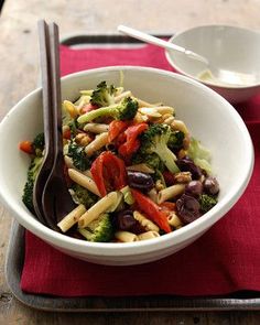 a white bowl filled with pasta and vegetables on top of a red place mat next to a fork