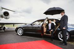 a man in a suit getting out of a car with an umbrella over his head