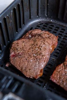 two steaks being cooked on the grill with seasoning sprinkled on them