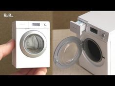 a hand is holding a small white washing machine next to a washer and dryer