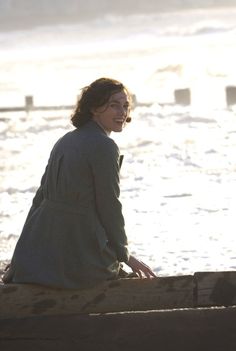 a woman sitting on top of a wooden bench next to the ocean