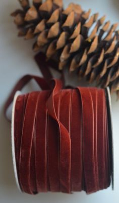 a roll of red velvet ribbon next to a pine cone