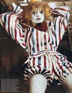 a woman with red and white stripes on her body wearing a clown mask, striped shirt and shorts