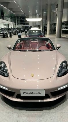 a pink sports car is parked in a showroom filled with other cars and people