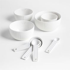 five white bowls and spoons on a white surface