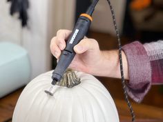 a person using a drill to paint a white pumpkin with black piping on it