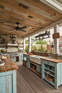 an outdoor kitchen with wooden floors and ceiling fans above the sink, counter tops and cabinets