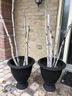 two black planters with white branches in front of a brick wall on a patio