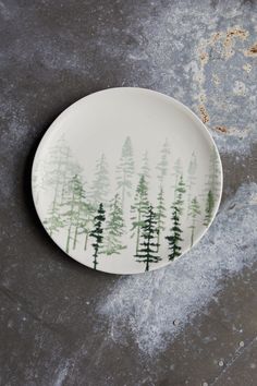 a plate with trees painted on it sitting on a table next to some snow covered ground