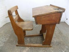 an old wooden school desk and chair sitting on concrete floor next to white brick wall