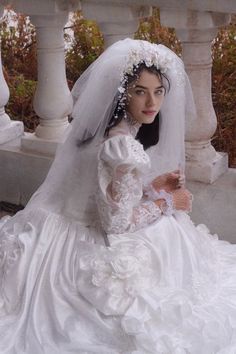 a woman in a white wedding dress sitting on a stone bench wearing a veil and tiara