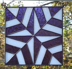 a purple and white stained glass window hanging from a metal chain on a tree branch