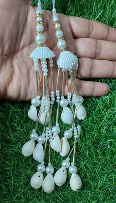 a pair of white sea shells and pearls dangle earrings in the palm of someone's hand