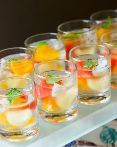 several glasses filled with different types of drinks on a white tray and one glass has fruit in it