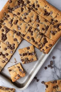 chocolate chip cookie bars cut into squares and placed on a baking sheet with more cookies scattered around