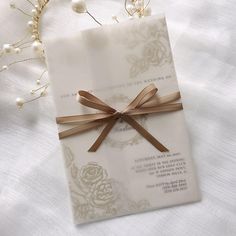 a white and gold wedding card with a brown ribbon on the front is laying on a bed