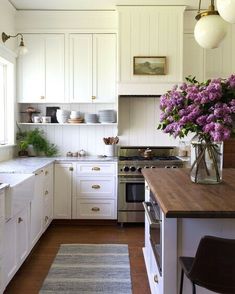 a kitchen with white cabinets and purple flowers in a vase on the counter top next to an oven