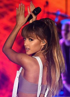 a woman with long hair and white overalls is holding her hand up in the air