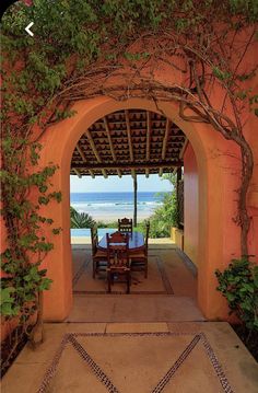 an outdoor dining area with orange walls and greenery on the outside, along with a wooden table set for four