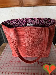 This designer bag is hand made by me and is one of a kind.  This bag is made of an orange crocodile faux leather and is lined with a pink leopard skin fabric designed by Ink & Arrow. There is a magnetic snap closure. The lining has eight pockets and there is lots of room inside. This is a gorgeous bag. The straps are sturdy and are long enough to drape over your shoulder when carrying.   The bag has many uses and is especially handy when you travel to far places. You will love it. Dimensions:  Bag - 19.5" W x 15" L x 5" D,  Shoulder Strap Clearance - 15" L  From my smoke free and pet free studio to you. Please ask questions. Thank you for browsing my shop. Quilted Pillow Covers, African Fabrics, Leopard Skin, Faux Leather Bag, Vegan Leather Bag, Quilted Pillow, Makeup Pouch, Gorgeous Bags, Pink Leopard