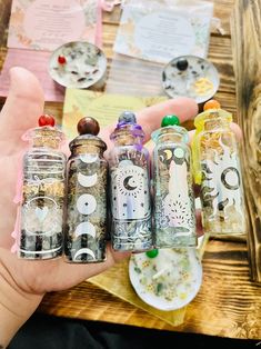 a person holding five small glass bottles in their hand with paper on the table behind them