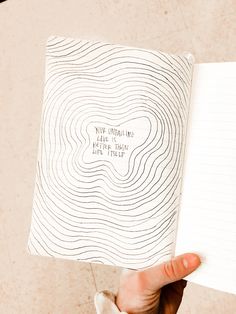 a person holding up a notebook with writing on the pages and an image of a wave