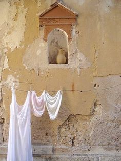 clothes hanging out to dry in front of a stone wall with a window and birdhouse