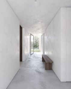 an empty hallway with white walls and concrete flooring, leading to a wooden bench