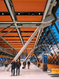 people are walking through an airport terminal with orange and white accents on the ceiling above them