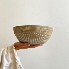 a person holding a bowl in their hand on a white surface with a wall behind them