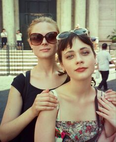 two women standing next to each other in front of a building