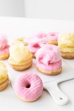 pink and yellow doughnuts are on a white tray next to a spatula