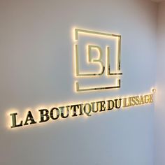 the logo for la boutique du usage is lit up in yellow and black letters on a white wall