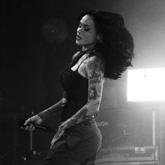 a woman with tattoos on her arm holding a microphone in front of a stage light