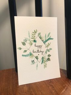 a card with the words happy birthday written in watercolor on it, sitting on top of a wooden table