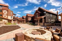 a fire pit in the middle of a courtyard surrounded by wooden buildings and stone patio furniture