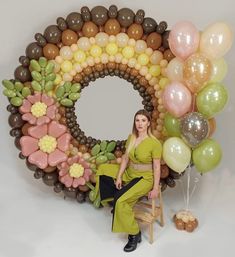 a woman sitting on a chair in front of balloons and wreaths that look like flowers