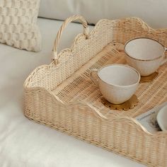 a wicker tray with two bowls and spoons in it sitting on a bed