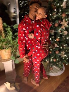 two people standing in front of a christmas tree wearing matching red and green pajama's