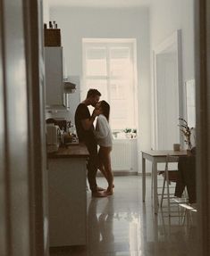 two people standing in a kitchen next to each other and one person kissing the other