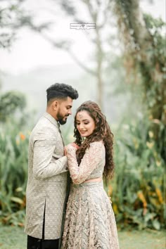 a man and woman standing next to each other in front of some trees with flowers