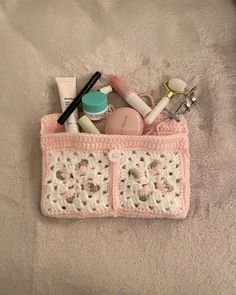 a pink crocheted purse filled with cosmetics and personal care items on top of a bed