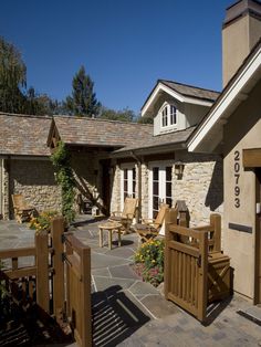 the outside of a house with wooden chairs and tables on it's patio area