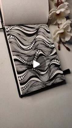 an artistically designed notebook sits on a table next to some flowers and a roll of toilet paper